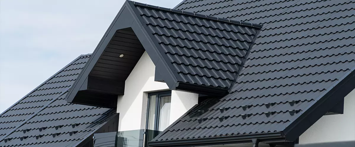A beautiful modern house is covered with black metal tiles. Roofing of metal profile wavy shape